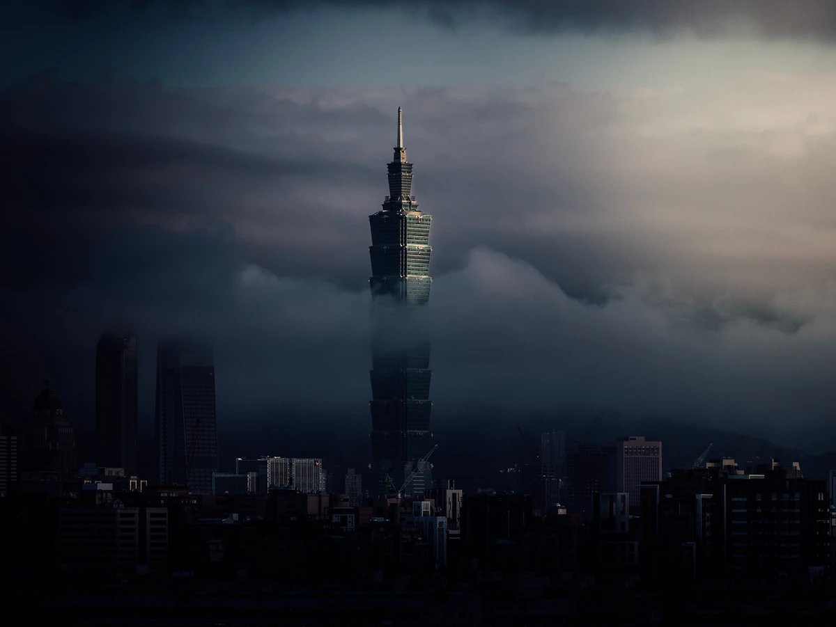 Taipei 101 rising out of low cloud above a dark city skyline.