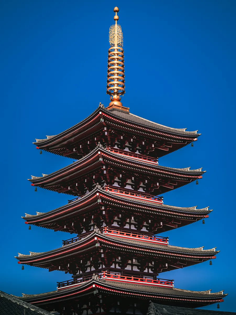 A five-storey pagoda with a gold spire and red-trimmed eaves against a deep blue morning sky.