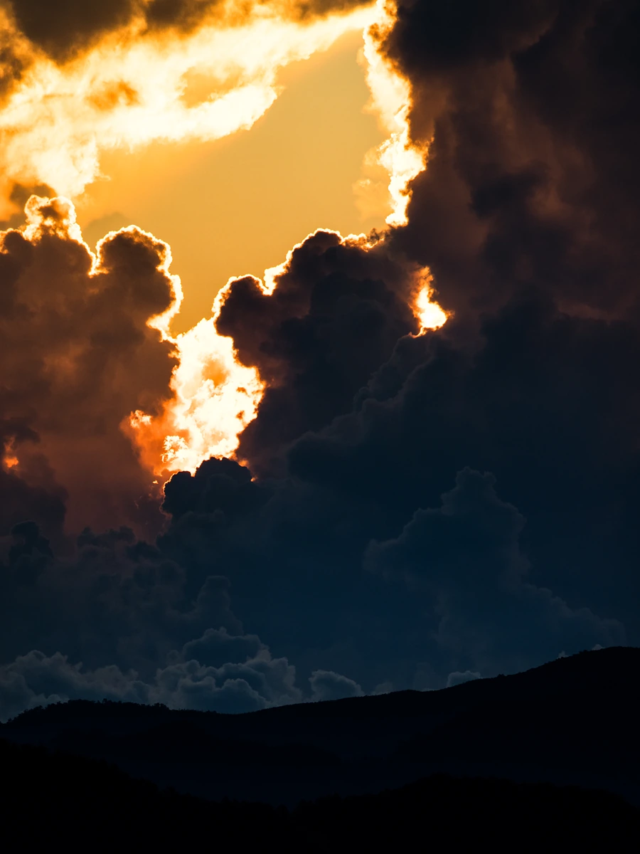 Towering storm clouds backlit gold above a dark mountain ridge.