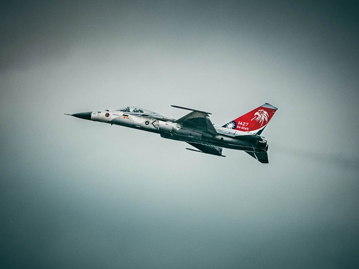 A grey fighter jet with a red, eagle-painted tail flies level against an overcast sky.