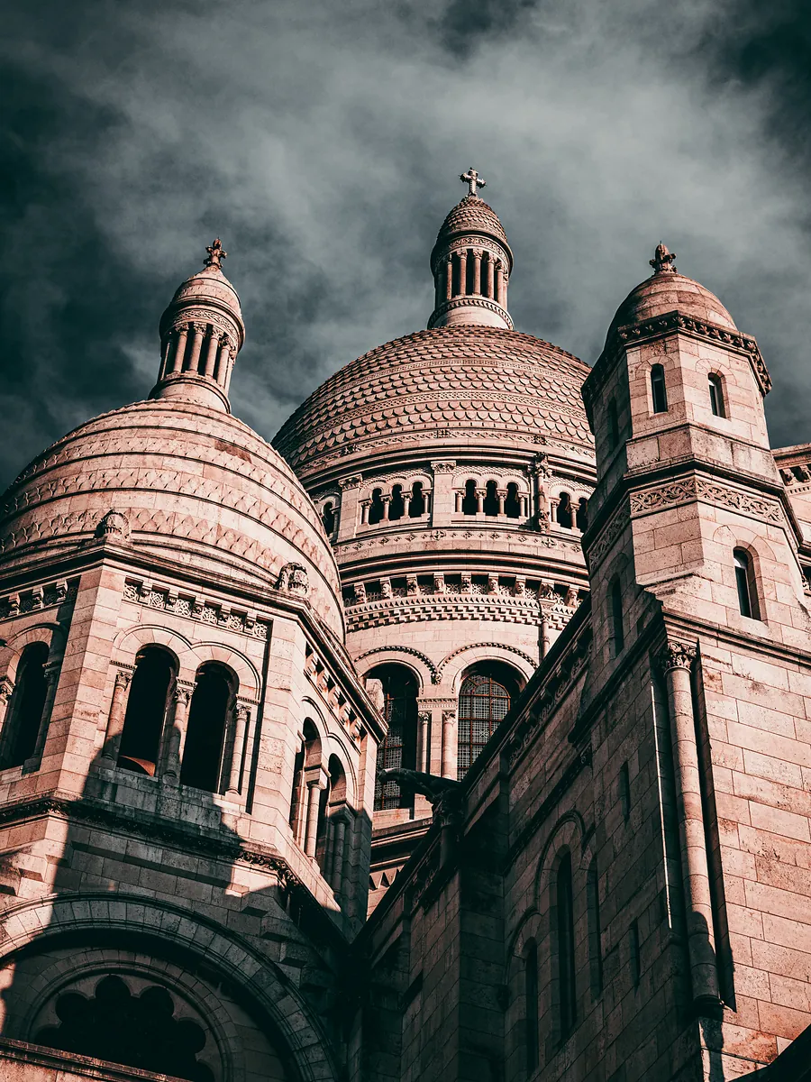 The domes of the Sacré-Cœur basilica in warm light under a dark, stormy sky.