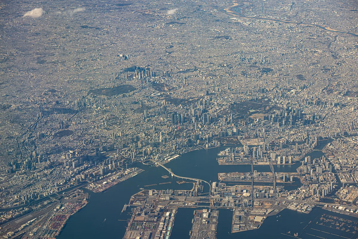 Aerial view of Tokyo's waterfront and Rainbow Bridge, the city spreading to the horizon.