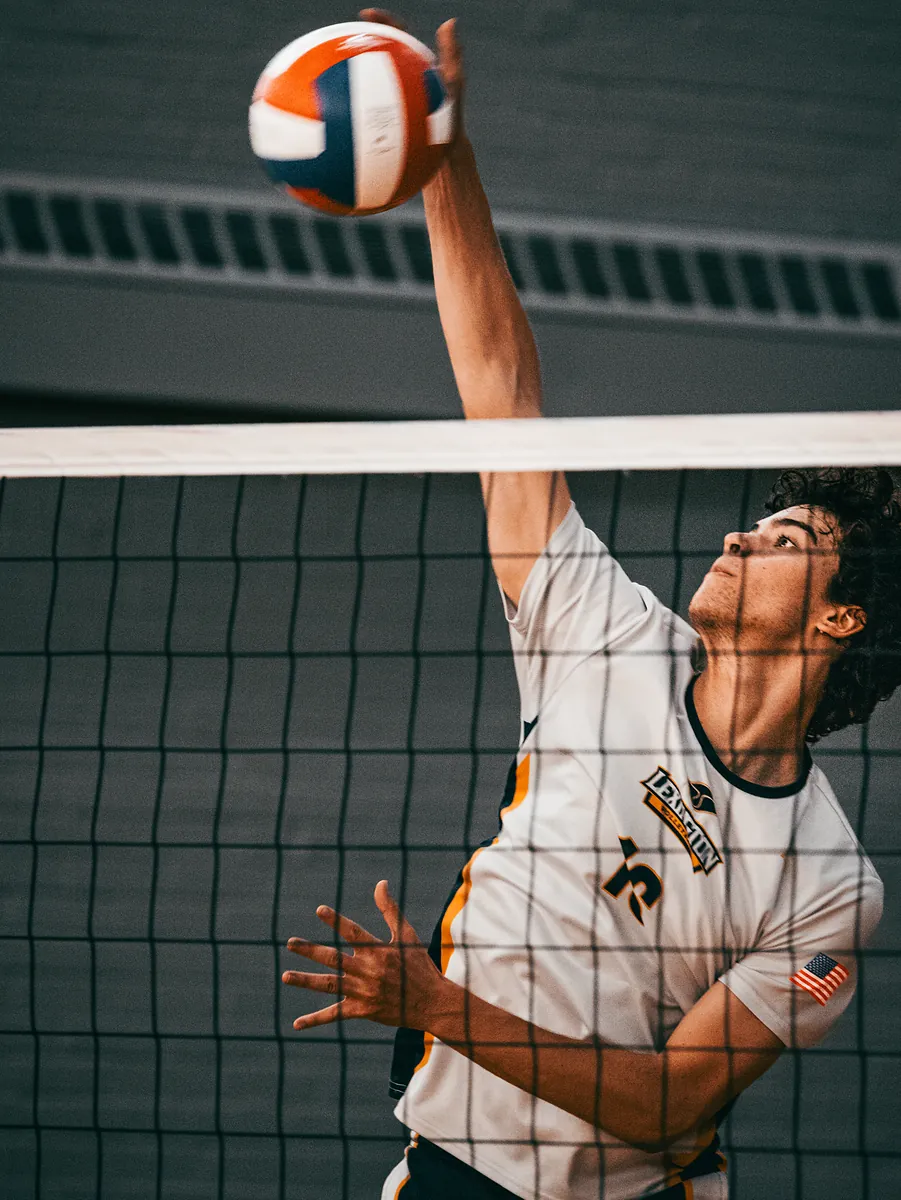 A volleyball player reaches high above the net to hit the ball.