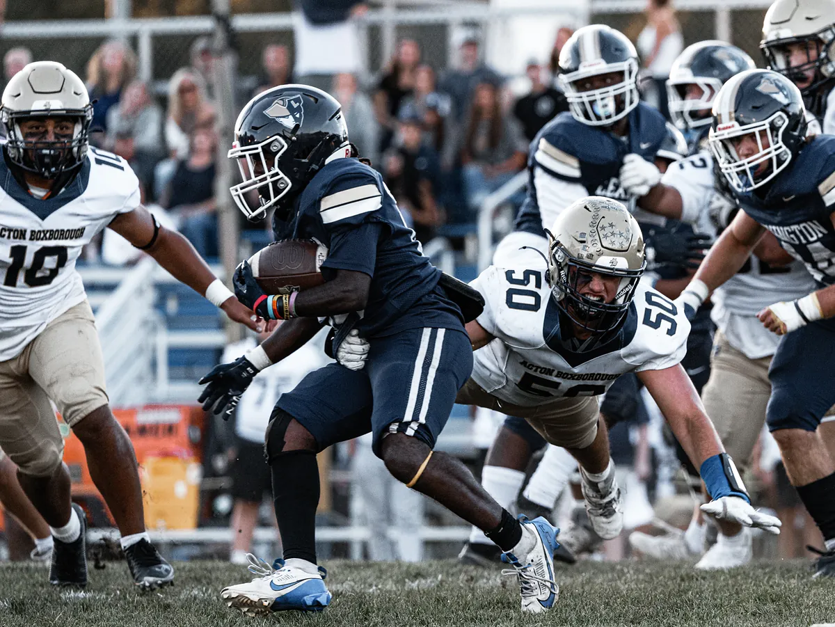 A ball carrier in navy drives through the line as a defender dives at his legs.