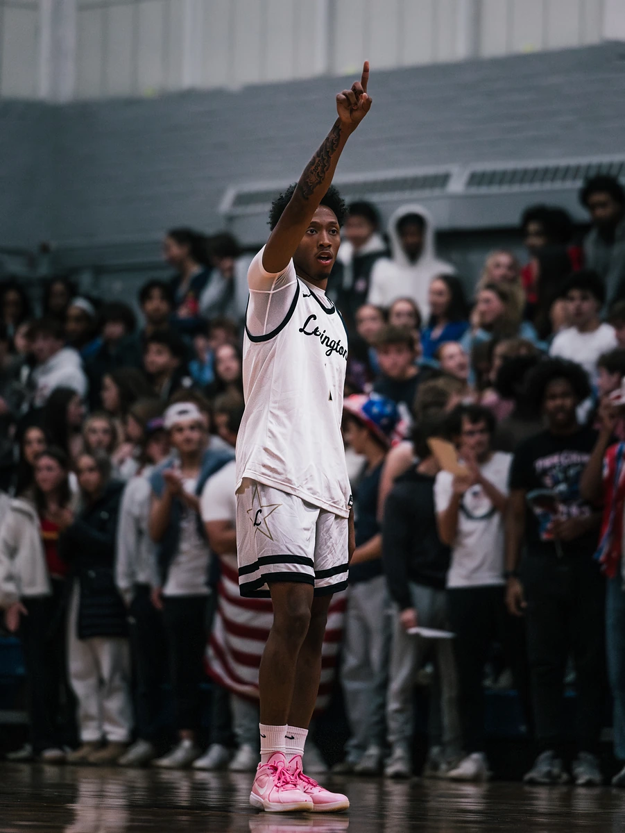 A basketball player in white raises one finger toward a crowd packed into the stands.