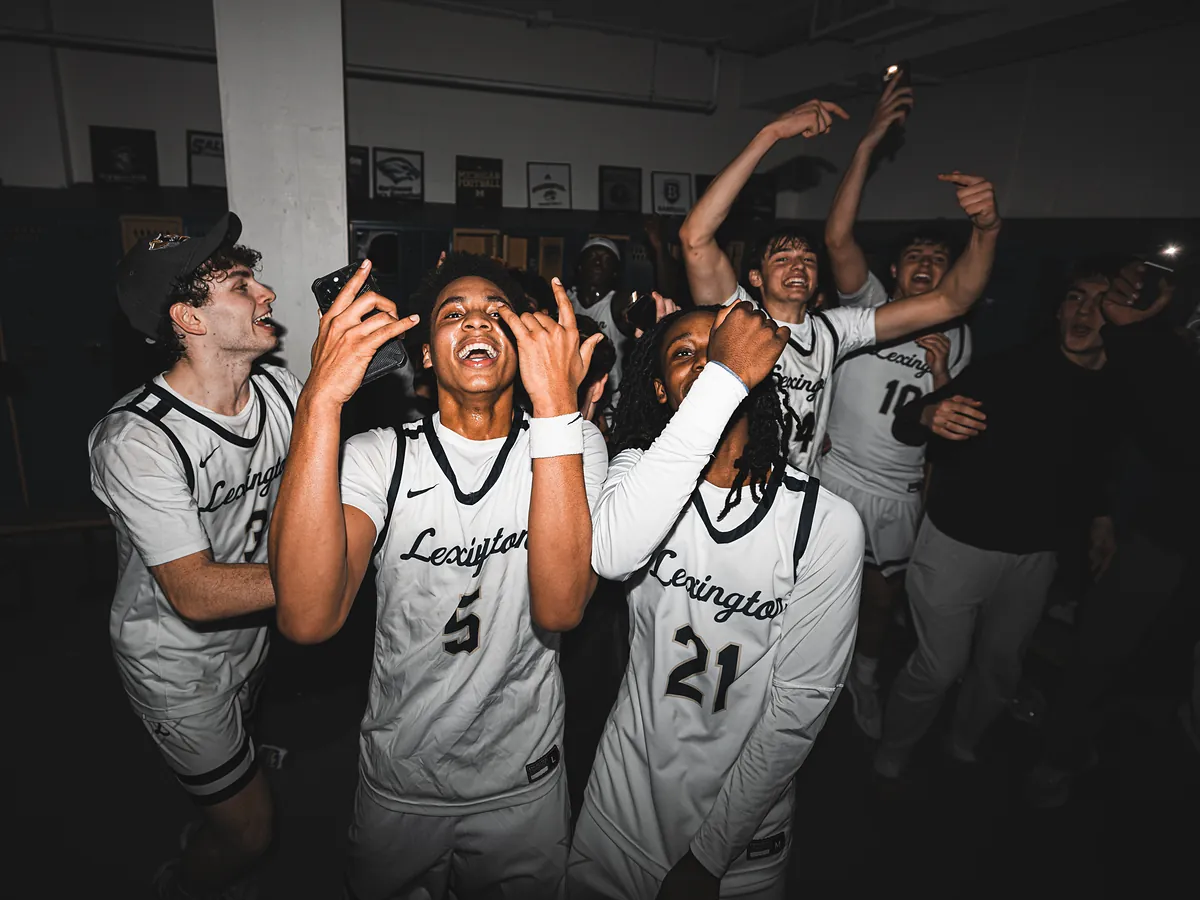 Players in white jerseys shout and point, filming the celebration on their phones.